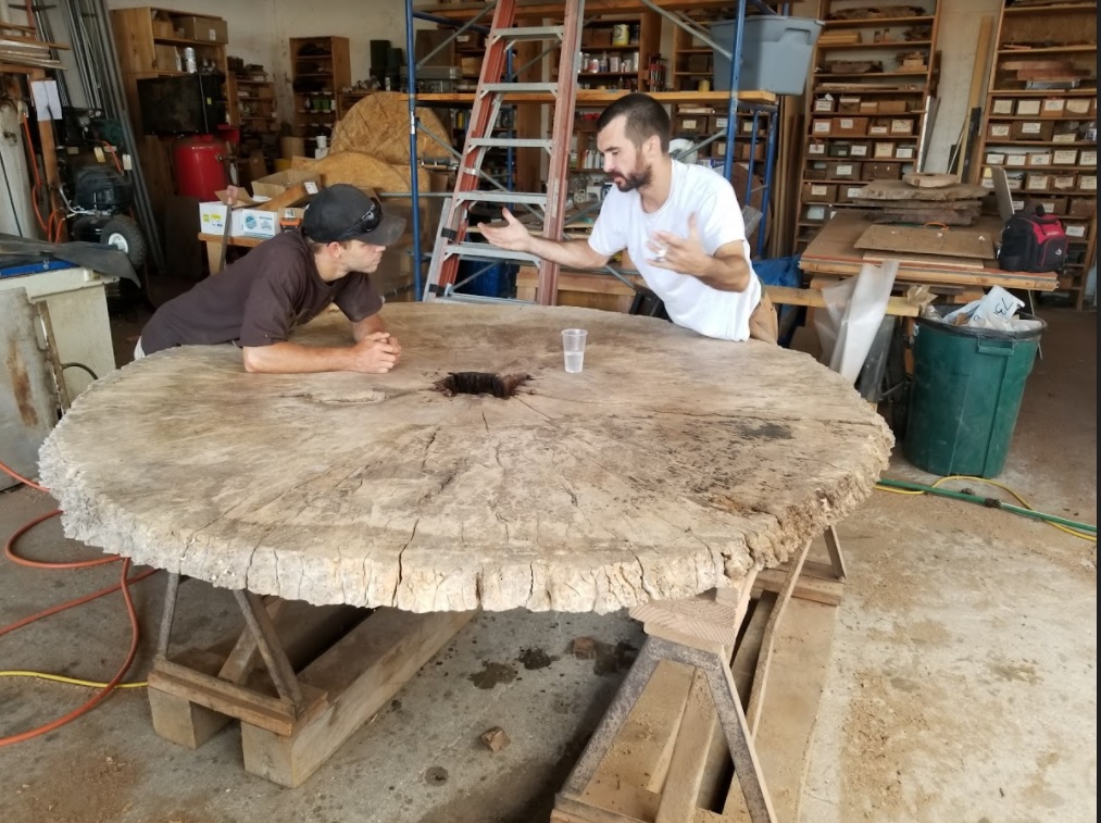 Two woodworkers standing around a large disc cut burl